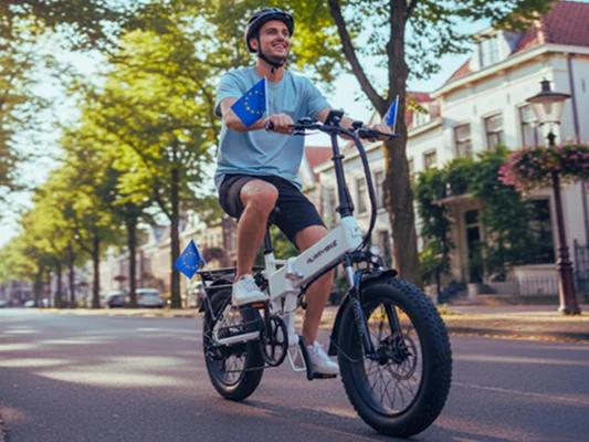 Man riding a white electric fat tire bike with blue flags attached to the handlebars on a European city street
