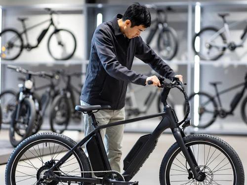 Man inspecting a black electric commuter bike in a bicycle store with display racks of e-bikes in the background