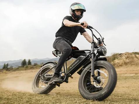 Man riding a black fat tire electric bike with a large headlight on a dirt field, kicking up dust