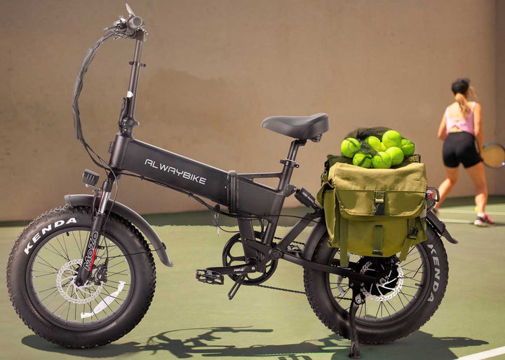 Black foldable fat tire electric bike with olive rear cargo bag full of tennis balls parked on outdoor tennis court, all-terrain folding ebike for sports commute