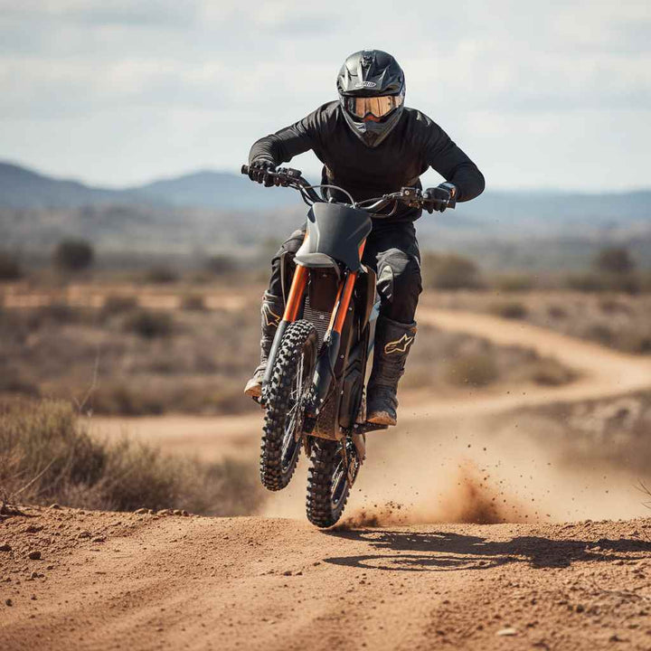 Off road rider performing a wheel lift on a black electric dirt bike on a dirt track