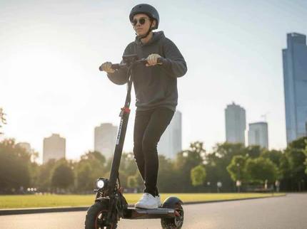 Young rider commuting on black Cemotoride electric scooter in city park with skyline background
