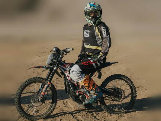 Motocross rider in full gear sitting on a black electric dirt bike on a sandy desert trail